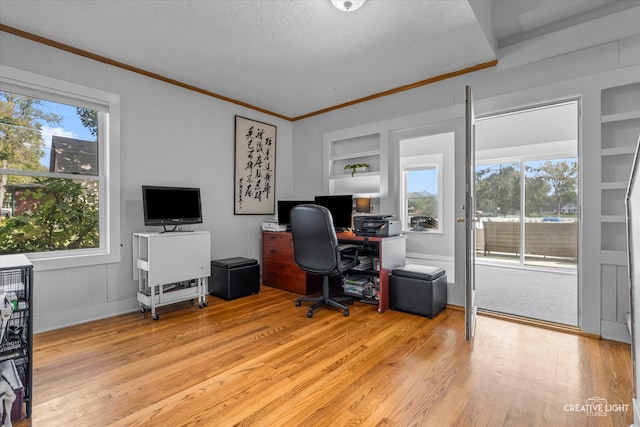 home office featuring a textured ceiling, light wood-type flooring, built in features, and crown molding