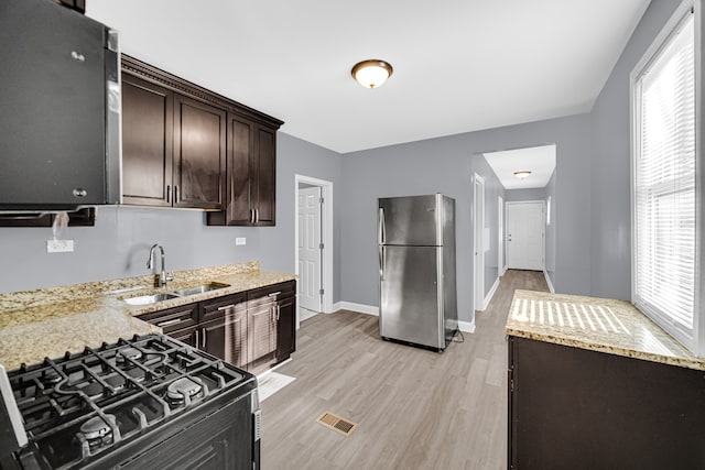 kitchen with light stone countertops, stainless steel fridge, gas range, sink, and light hardwood / wood-style floors