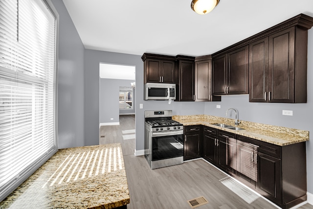 kitchen with light stone countertops, light wood-type flooring, dark brown cabinetry, stainless steel appliances, and sink