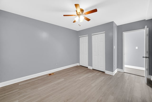 unfurnished bedroom featuring ceiling fan, light hardwood / wood-style floors, and two closets