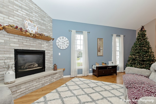 living room featuring light hardwood / wood-style floors, vaulted ceiling, and a brick fireplace