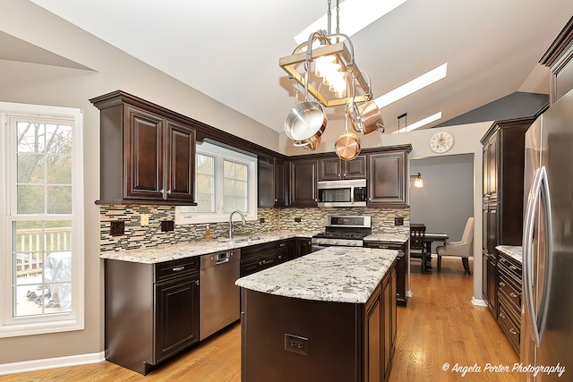 kitchen featuring stainless steel appliances, lofted ceiling with skylight, decorative light fixtures, a kitchen island, and light wood-type flooring