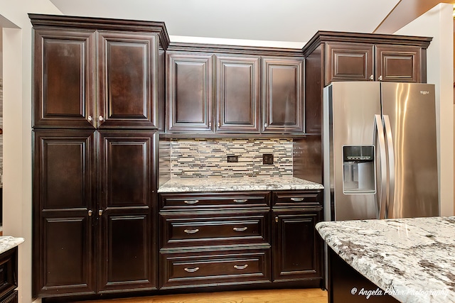 kitchen featuring decorative backsplash, stainless steel refrigerator with ice dispenser, light wood-type flooring, light stone counters, and dark brown cabinets