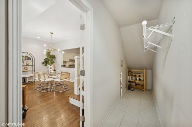 corridor featuring baseboards, a chandelier, and light wood-type flooring