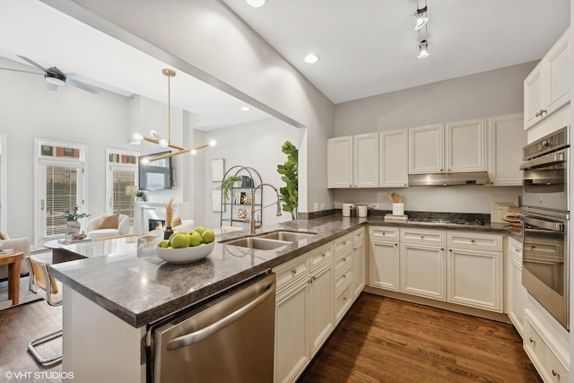 kitchen featuring a sink, under cabinet range hood, appliances with stainless steel finishes, pendant lighting, and a peninsula