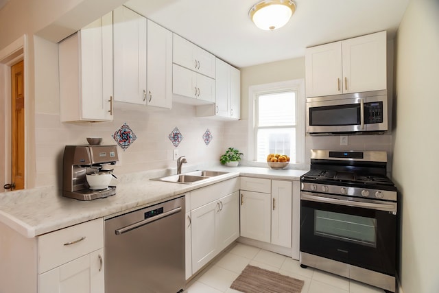 kitchen with decorative backsplash, appliances with stainless steel finishes, sink, light tile patterned floors, and white cabinets