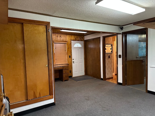 foyer featuring dark carpet, a textured ceiling, and wooden walls