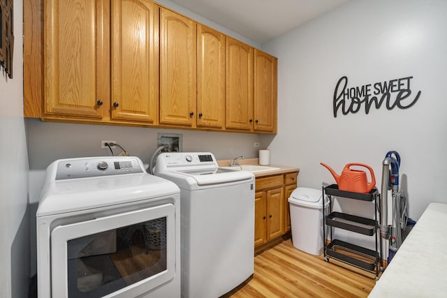 washroom featuring cabinets, washer and clothes dryer, sink, and light hardwood / wood-style flooring