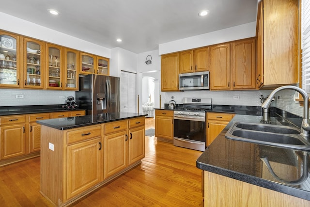 kitchen featuring appliances with stainless steel finishes, sink, decorative backsplash, a center island, and light wood-type flooring