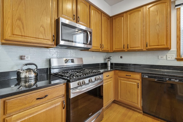 kitchen with dark stone countertops, tasteful backsplash, stainless steel appliances, and light wood-type flooring