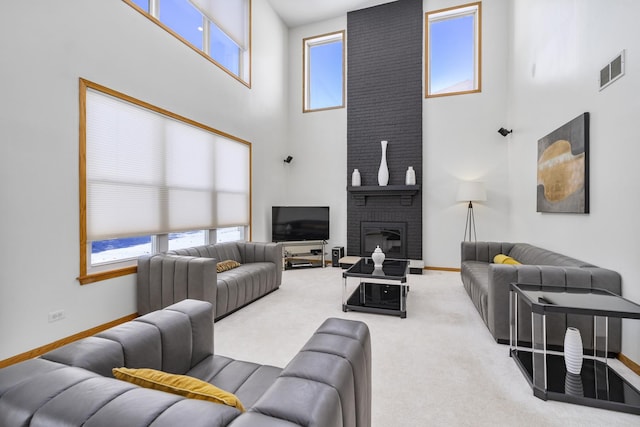 carpeted living room with a brick fireplace, a healthy amount of sunlight, and a towering ceiling