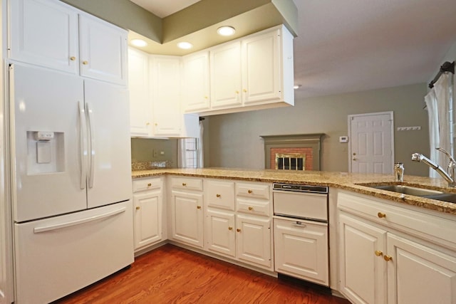 kitchen with wood finished floors, a peninsula, white fridge with ice dispenser, white cabinetry, and a sink