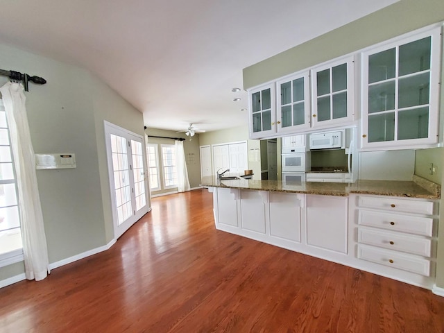 kitchen with stone counters, glass insert cabinets, white cabinets, wood finished floors, and white appliances