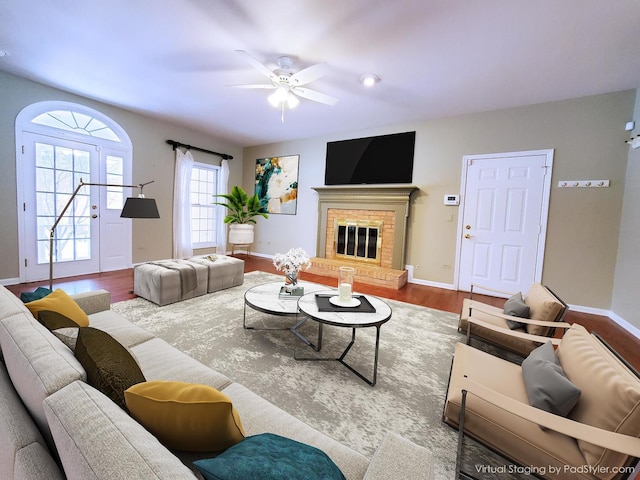 living area featuring a ceiling fan, a fireplace, baseboards, and wood finished floors