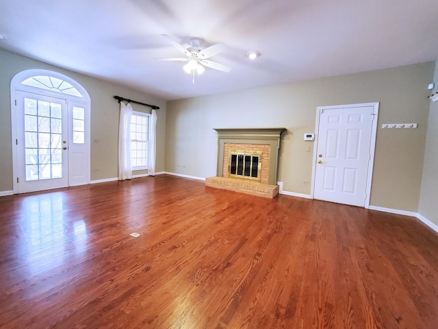 unfurnished living room with a fireplace, wood finished floors, a ceiling fan, and baseboards