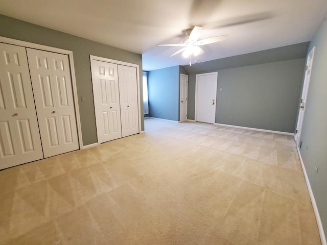 unfurnished bedroom with light carpet, baseboards, and two closets