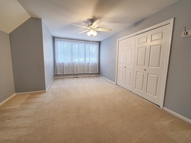 unfurnished bedroom with baseboards, light colored carpet, lofted ceiling, ceiling fan, and a closet