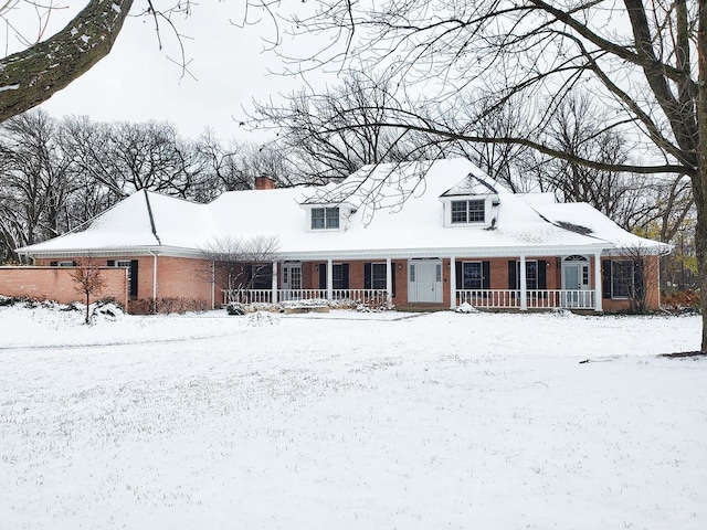 cape cod home featuring covered porch and brick siding