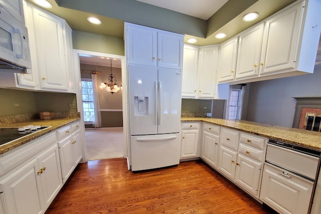 kitchen featuring white appliances, light wood finished floors, white cabinets, a peninsula, and an inviting chandelier