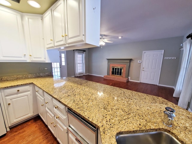 kitchen featuring white cabinets, open floor plan, a peninsula, a brick fireplace, and a sink