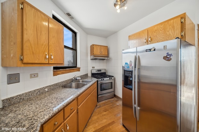 kitchen featuring sink, dark stone countertops, light hardwood / wood-style floors, decorative backsplash, and appliances with stainless steel finishes