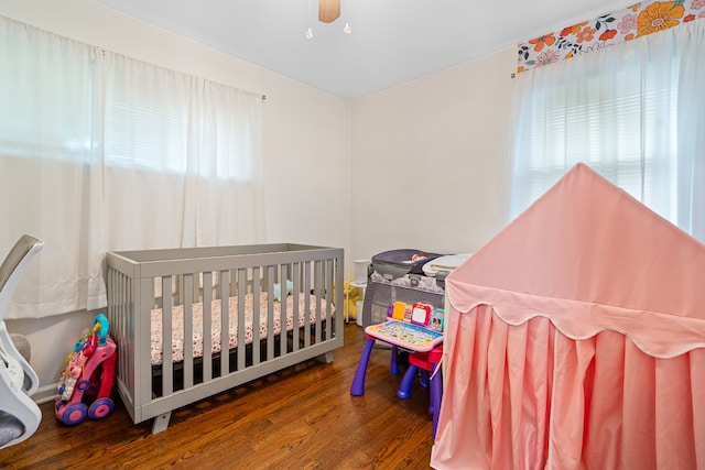 bedroom with ceiling fan, a nursery area, and dark hardwood / wood-style floors