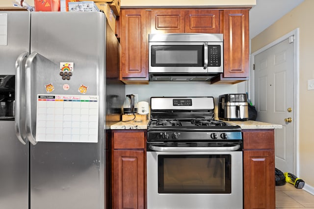 kitchen with tile patterned floors, light stone countertops, and appliances with stainless steel finishes