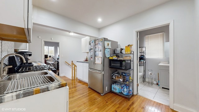 kitchen featuring white cabinetry, sink, stainless steel refrigerator, and light hardwood / wood-style flooring