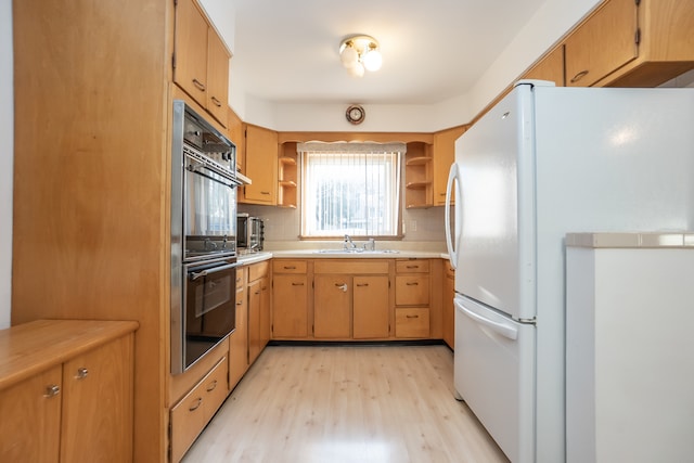 kitchen with decorative backsplash, light wood-type flooring, black double oven, sink, and white refrigerator