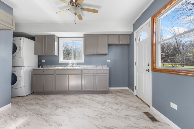 kitchen featuring ceiling fan, sink, stacked washing maching and dryer, crown molding, and gray cabinets