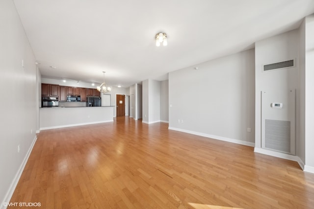 unfurnished living room featuring a chandelier and light hardwood / wood-style floors