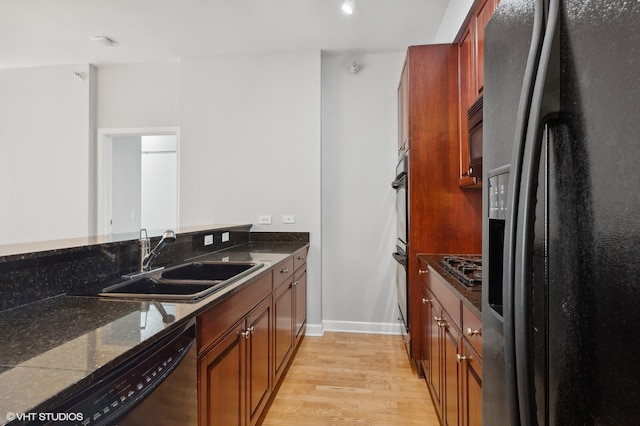 kitchen featuring light wood-type flooring, sink, dark stone countertops, and black appliances