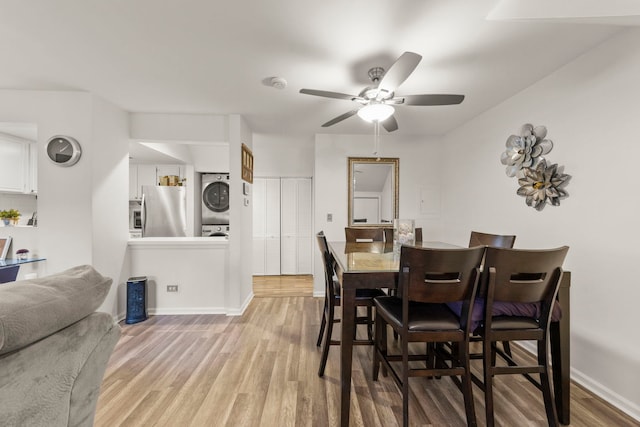 dining room featuring light wood-type flooring, stacked washer / dryer, and ceiling fan