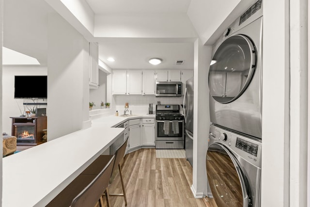 kitchen featuring appliances with stainless steel finishes, sink, light hardwood / wood-style flooring, white cabinetry, and stacked washer / drying machine