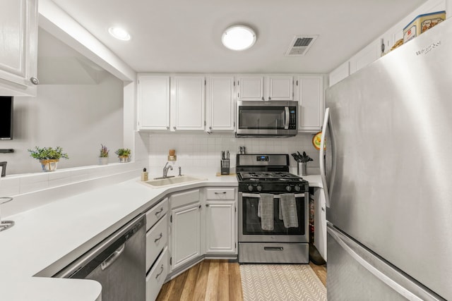 kitchen featuring white cabinetry, sink, light hardwood / wood-style floors, decorative backsplash, and appliances with stainless steel finishes