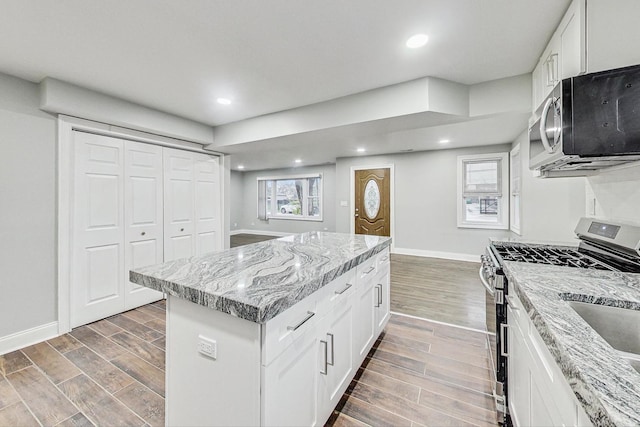 kitchen featuring white cabinets, a center island, light stone counters, and stainless steel gas range