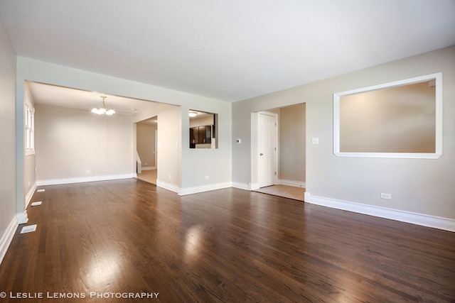 spare room featuring dark wood-type flooring and a notable chandelier