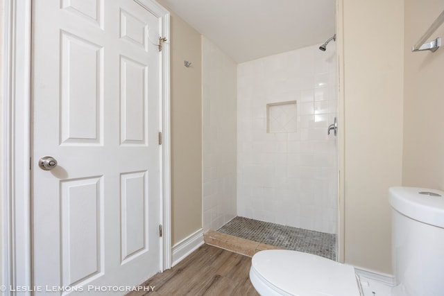 bathroom with tiled shower, toilet, and hardwood / wood-style flooring