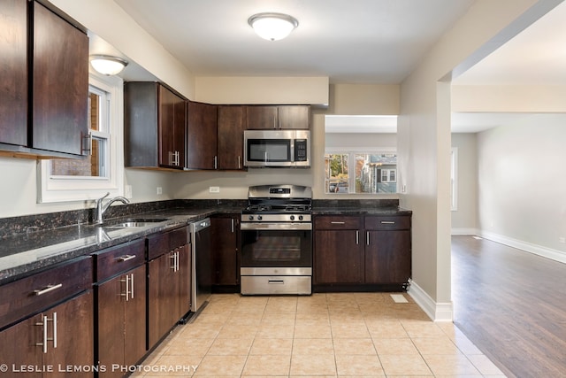 kitchen with sink, dark stone countertops, dark brown cabinets, light hardwood / wood-style floors, and stainless steel appliances