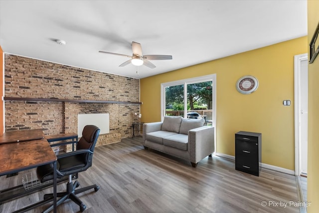 home office with ceiling fan, wood-type flooring, and brick wall