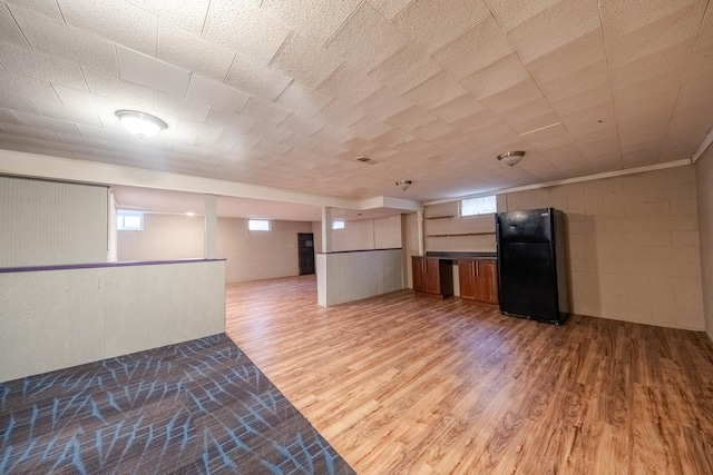 basement featuring black refrigerator, light hardwood / wood-style floors, and plenty of natural light