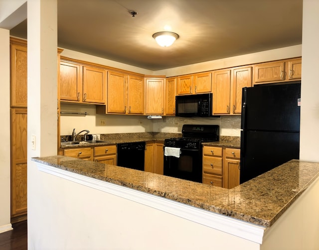 kitchen featuring sink, dark hardwood / wood-style floors, kitchen peninsula, dark stone countertops, and black appliances