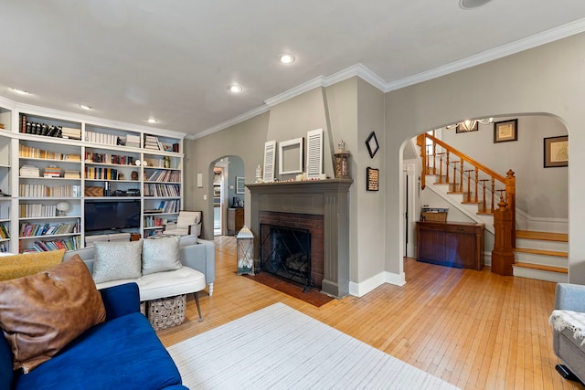 living room featuring a brick fireplace, ornamental molding, and light wood-type flooring