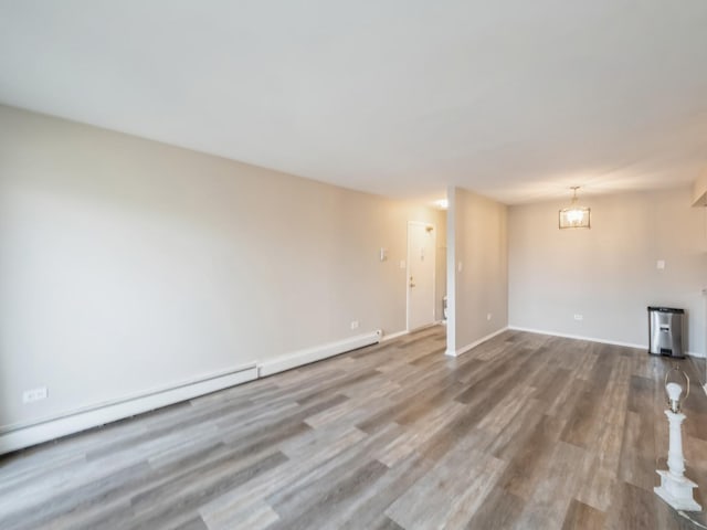 empty room with hardwood / wood-style flooring, a chandelier, and a baseboard heating unit