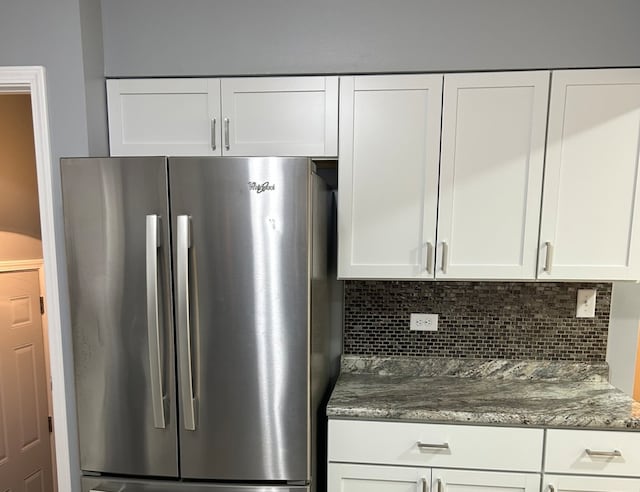 kitchen with white cabinets, backsplash, stainless steel refrigerator, and dark stone countertops