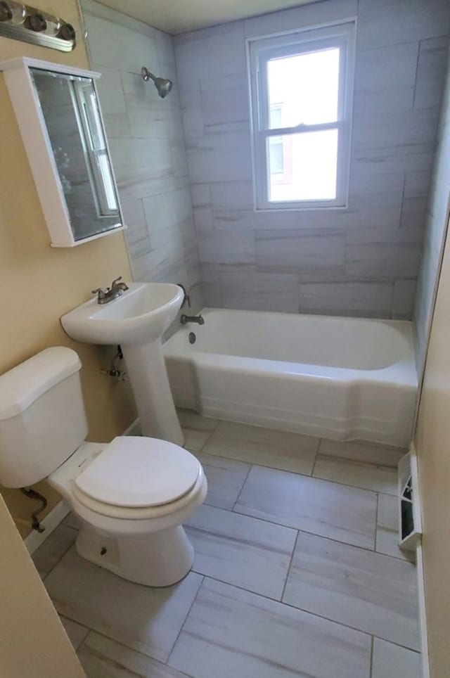 bathroom with tile patterned flooring, toilet, and tiled shower / bath