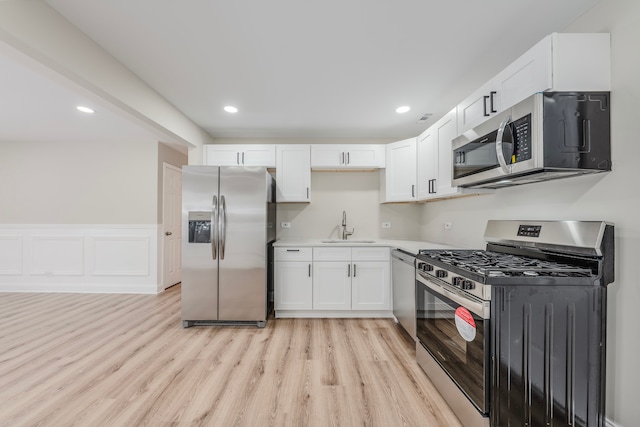 kitchen with white cabinets, appliances with stainless steel finishes, light hardwood / wood-style flooring, and sink