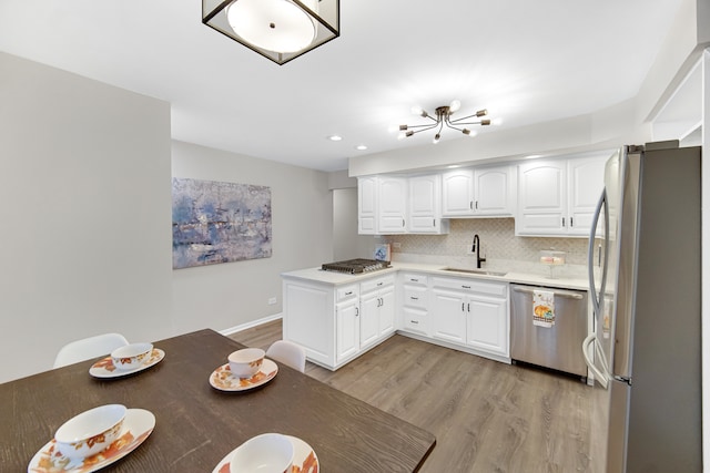 kitchen featuring light wood-type flooring, backsplash, stainless steel appliances, sink, and white cabinets