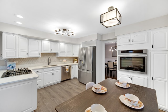 kitchen featuring backsplash, white cabinets, sink, light hardwood / wood-style floors, and stainless steel appliances