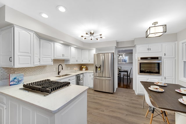 kitchen featuring kitchen peninsula, light wood-type flooring, stainless steel appliances, sink, and white cabinets